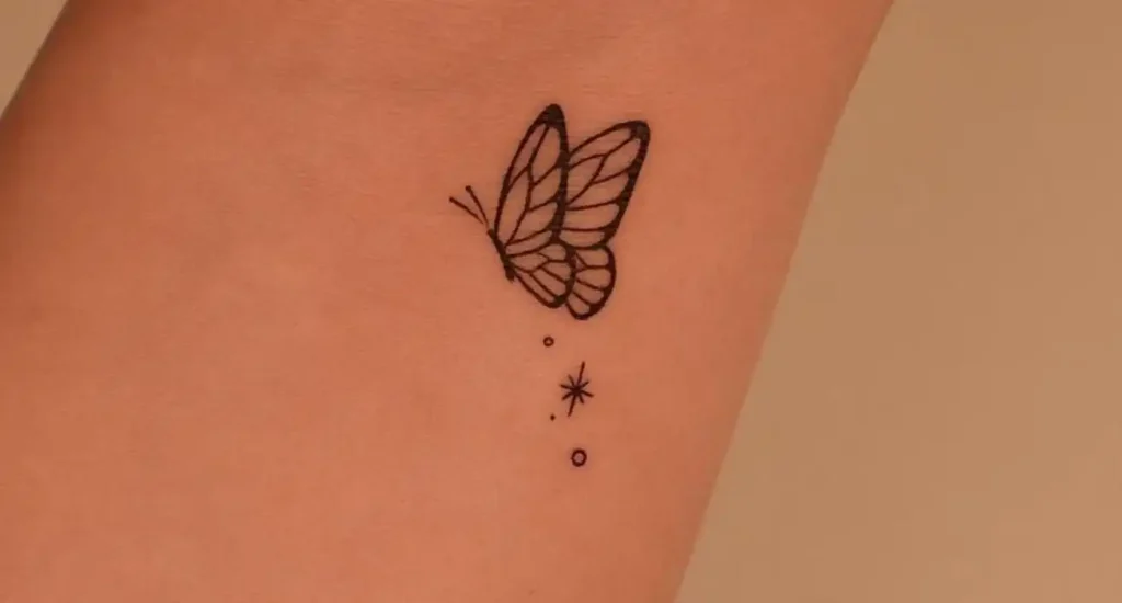 A small, delicate butterfly tattoo with a minimalist star and circles on the inner arm.